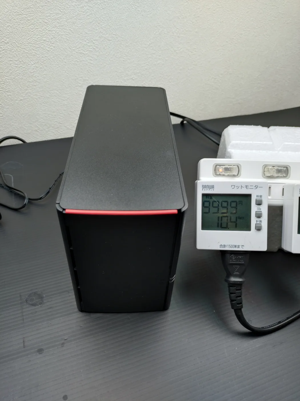サンワサプライのワットモニターがBuffalo LinkStation LS220D0802Gのアイドル時消費電力10.4Wを表示している様子。左は黒い本体で前面に赤いラインが入っている